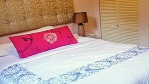 A neatly made bed with a white and blue patterned bedspread, a red pillow with a floral design, a bedside lamp, and a patterned wall. - Private Garden Villa in Manchester's Cool Highlands  (Cross keys)