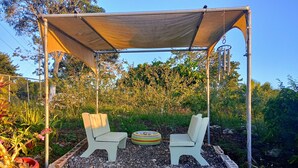 A covered outdoor seating area with two chairs and a round table, surrounded by potted plants and gravel. - Private Garden Villa in Manchester's Cool Highlands  (Cross keys)