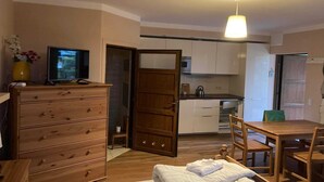 A compact room with a wooden dresser, a bed, a dining table with chairs, a television, and a kitchen area with cabinets and appliances. - Cozy 3-person apartment, Pobierowo (Pobierowo)