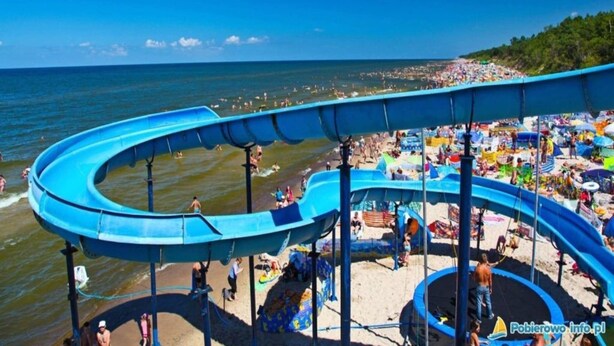 A water slide at a beach with a view of the ocean and a crowded beach area. - Cozy 3-person apartment, Pobierowo (Pobierowo)