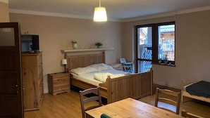 Quarto com cama de madeira, mesa de cabeceira, abajur e televisão em uma cômoda. Há uma janela com vista para um edifício.