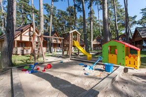 A playground with a slide, swings, and sand area, surrounded by wooden cabins. - Apartment in Pobierowo near Baltic Beach (Pobierowo)