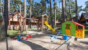 A playground with a slide, swings, and sand area, surrounded by wooden cabins. - Apartment in Pobierowo near Baltic Beach (Pobierowo)
