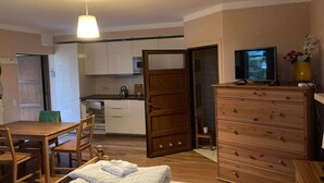 A compact room with a wooden dining table, chairs, a bed, a wooden dresser, a television, and a kitchen area with cabinets and a microwave. - Apartment in Pobierowo near Baltic Beach (Pobierowo)