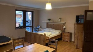 A room with a bed, a desk, a chair, a TV, a cabinet, and a window with a view of a building. - Apartment in Pobierowo near Baltic Beach (Pobierowo)