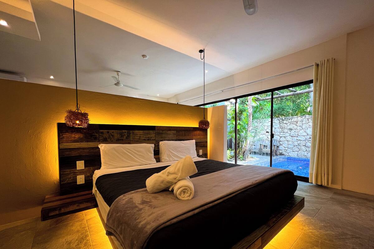 Un dormitorio moderno con una cama grande, cabecera de madera y vistas a un jardín a través de una puerta corrediza de vidrio.