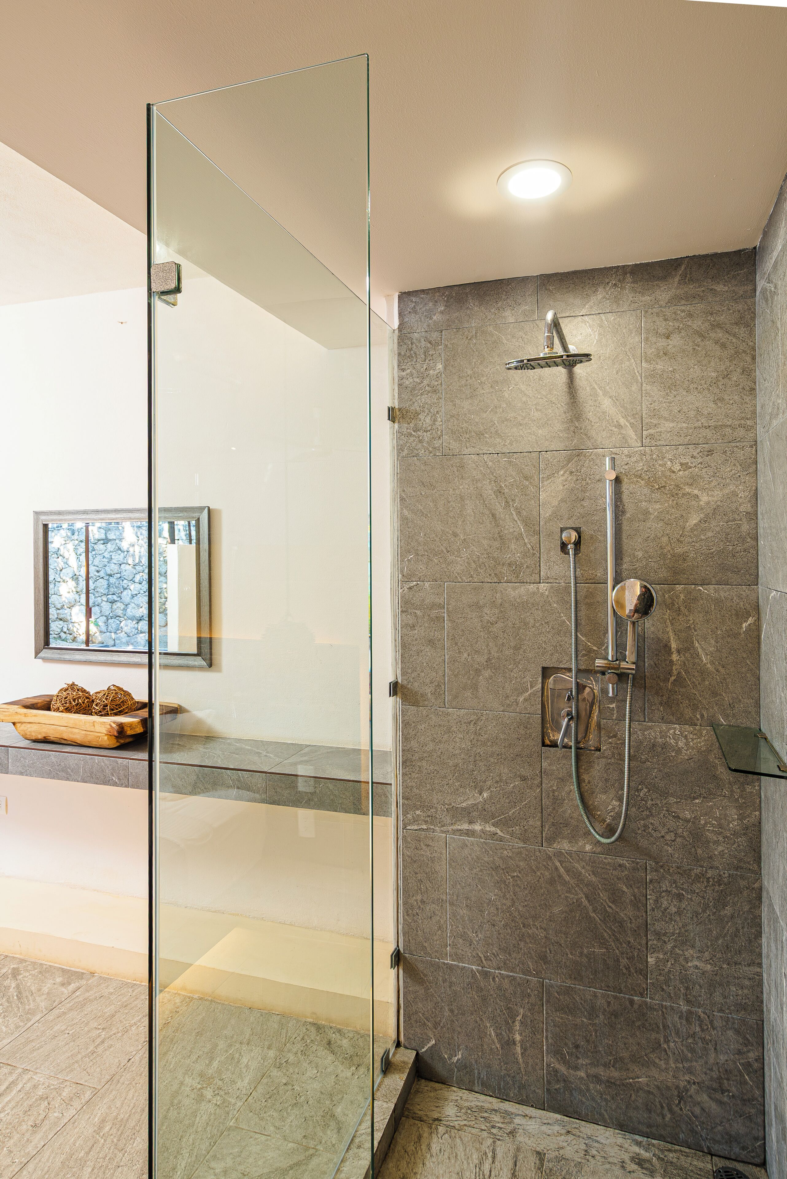 A modern bathroom with a glass shower enclosure, a marble-tiled shower area, and a wooden tray with decorative items.