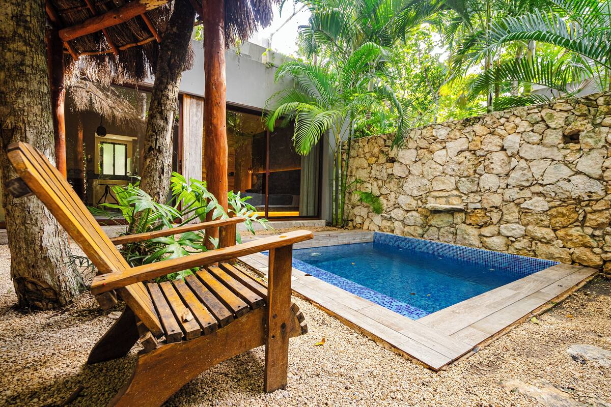 Una silla de lounge de madera, un muro de piedra y una piscina.