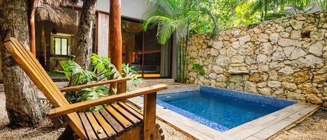 A wooden lounge chair, a stone wall, and a swimming pool.