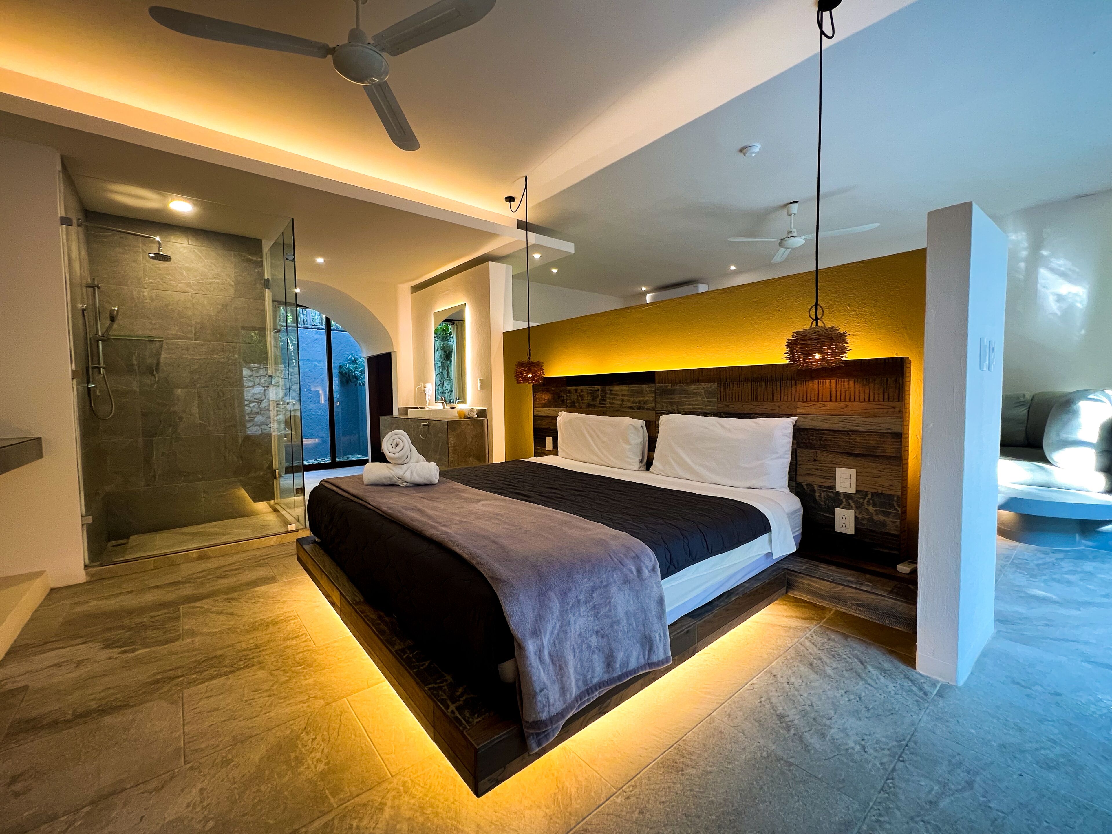 A modern bedroom with a large bed, a walk-in shower, and a view of the outdoors.