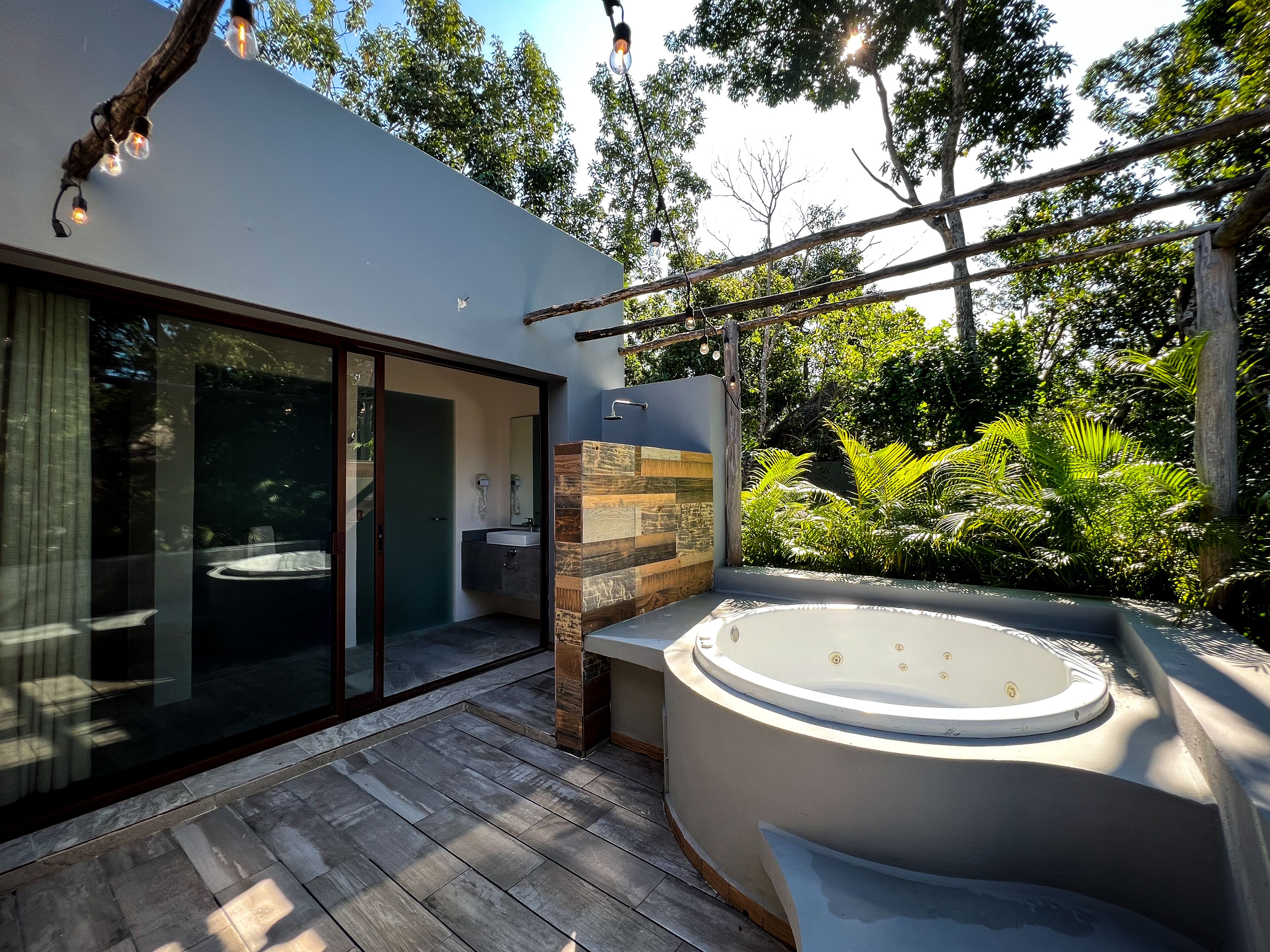 Une salle de bain moderne en plein air, dotée d’un jacuzzi, d’une terrasse en bois et d’une porte en verre donnant sur une zone de piscine.