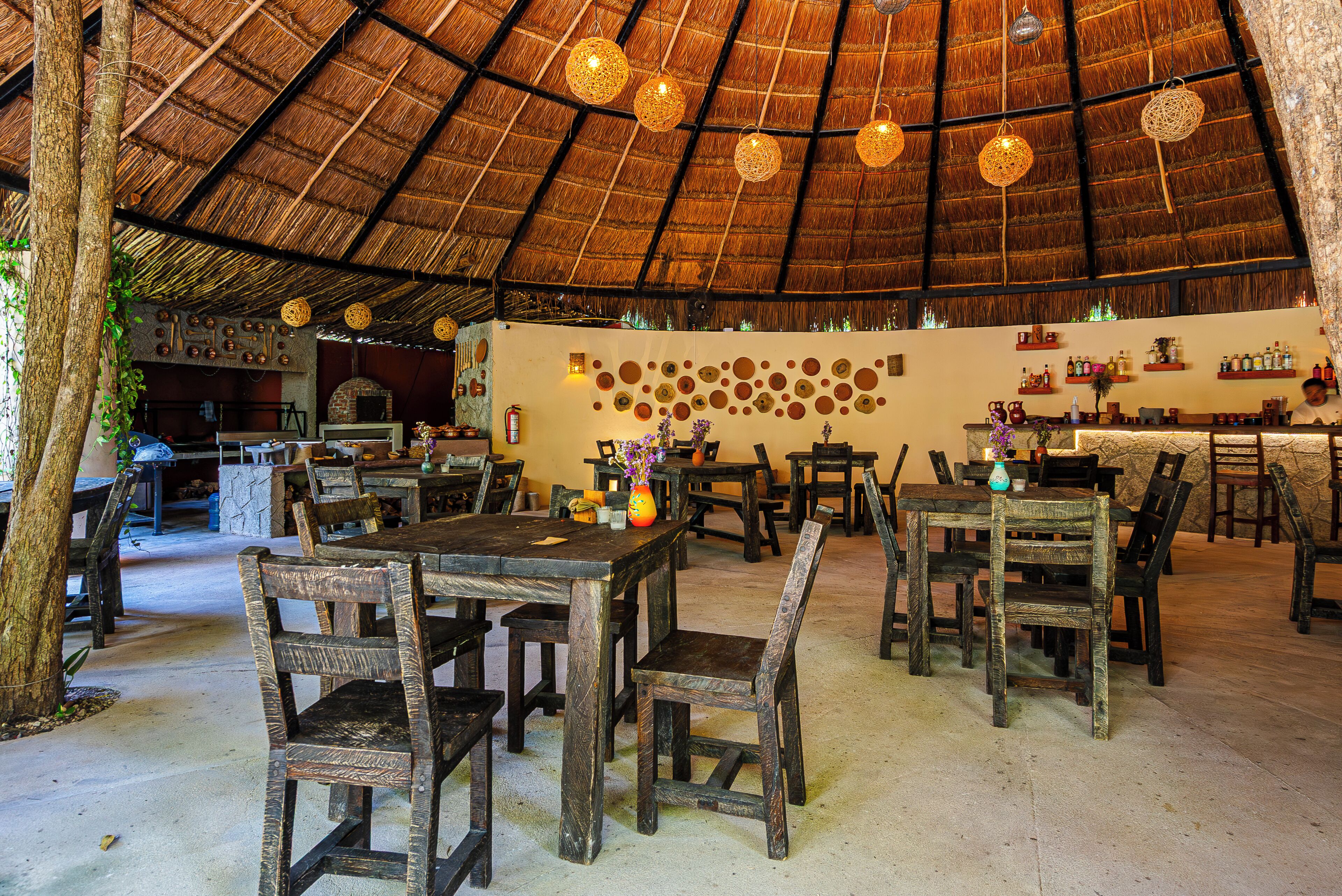 Un comedor interior con techo de paja, mesas y sillas de madera.