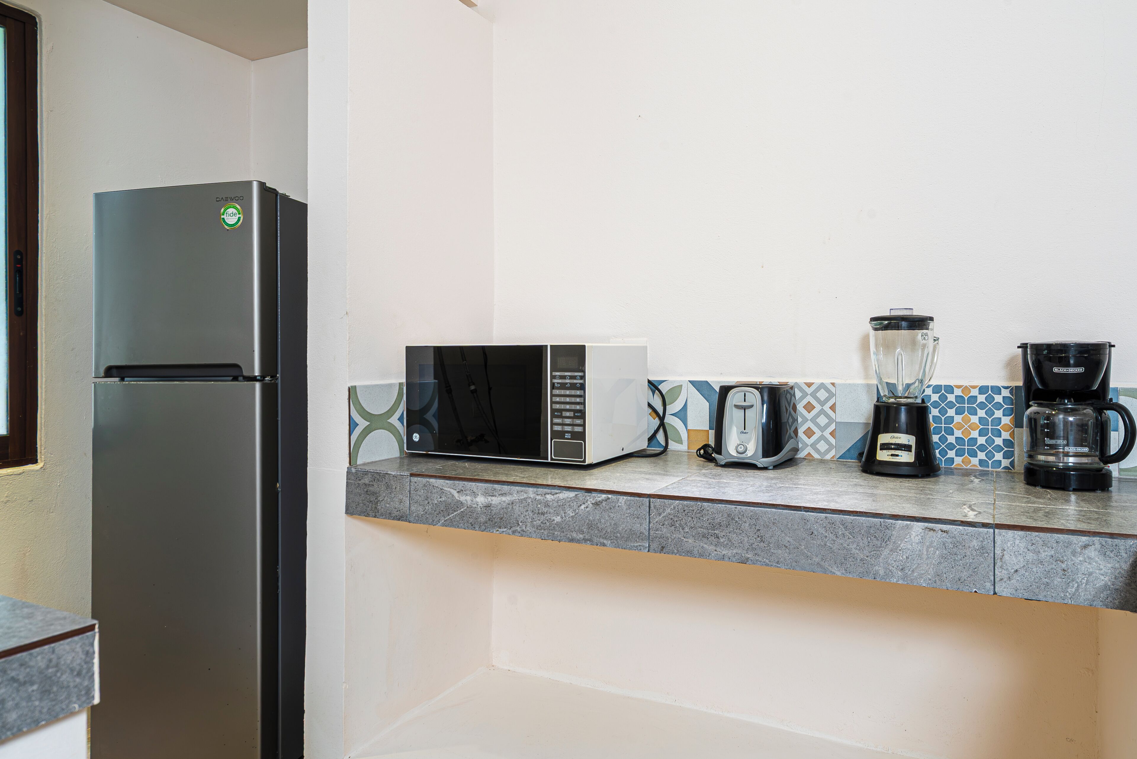 A kitchen with a refrigerator, microwave, toaster, blender, and coffee maker on the countertop.