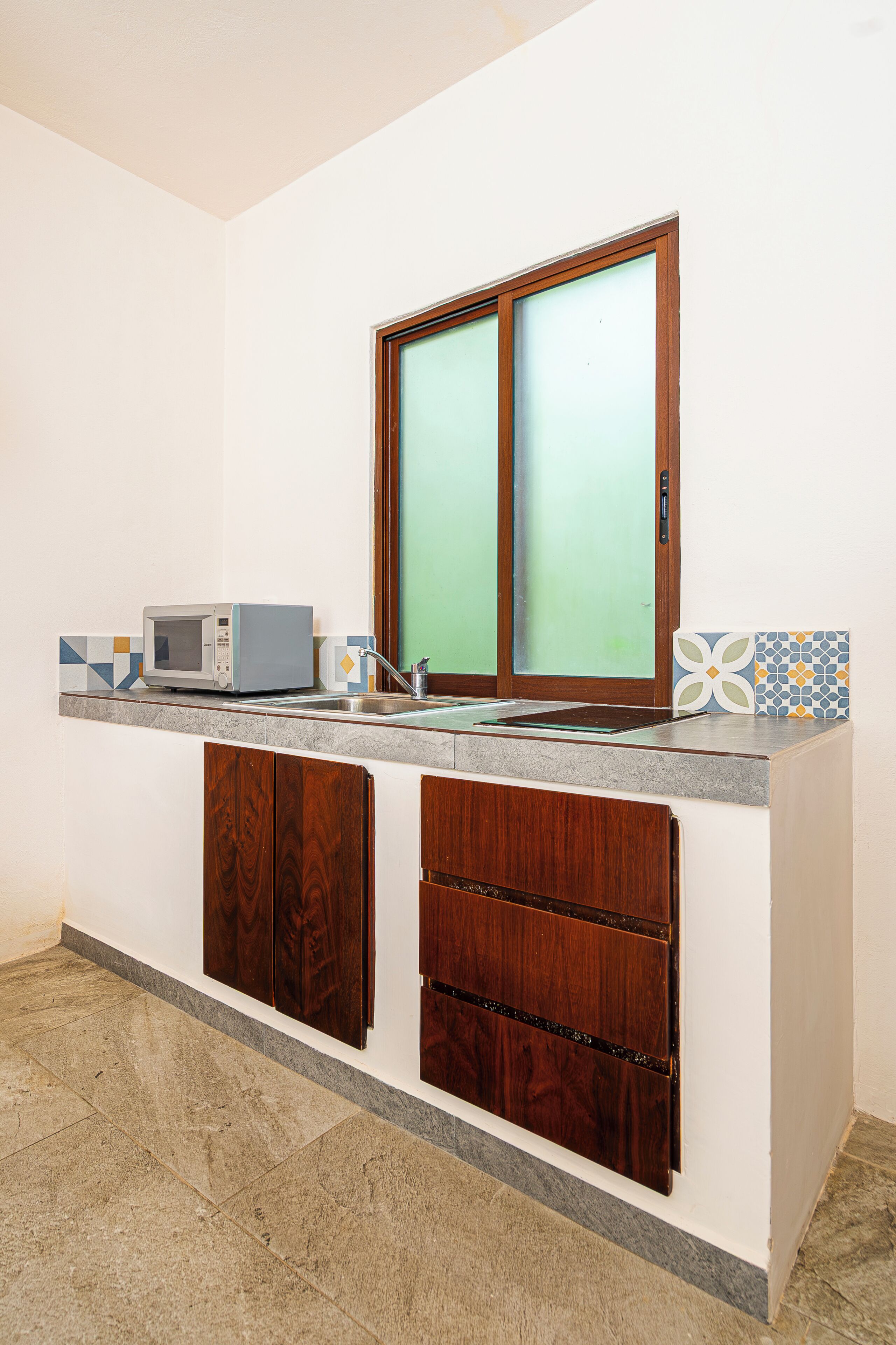 Una cocina con microondas, armarios de madera, un lavaplatos y una ventana con vidrio esmerilado.
