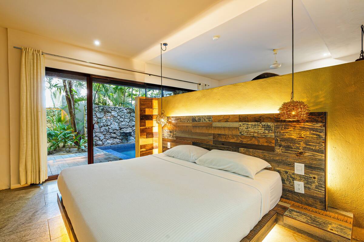 Un dormitorio moderno con una cama grande, una pared de piedra y vistas a un jardín tropical.