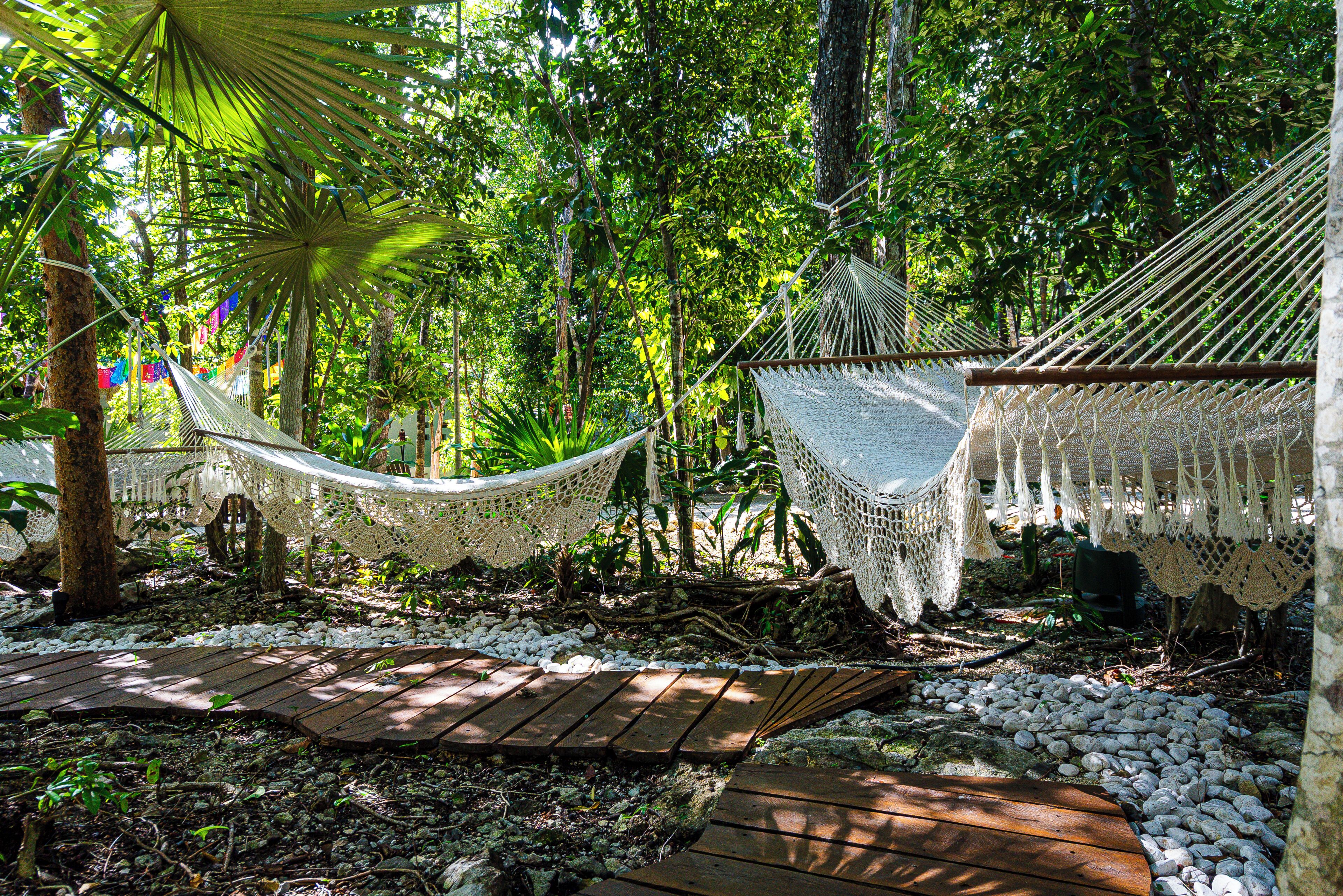 A hammock in a forested area with a wooden deck and white pebbles.