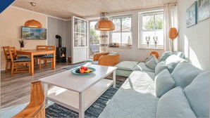 A cozy living room with a sofa, dining table, and chairs, a fireplace, and large windows. - Ferienwohnung mit Kamin am Achterwasser in Lütow (Lütow)