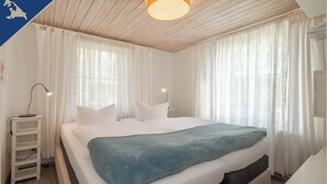 A bedroom with a bed, white curtains, a bedside lamp, and a wooden ceiling. - Ferienwohnung mit Kamin am Achterwasser in Lütow (Lütow)