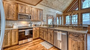 A modern kitchen with wooden cabinetry, stainless steel appliances, and large windows offering views of the outdoors. - Sunglow Mt Vista - Pet friendly-Mountain View- Hottub-  (Cherrylog)