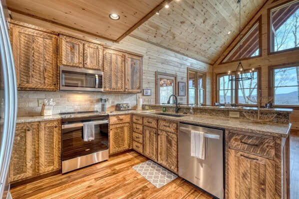 A modern kitchen with wooden cabinetry, stainless steel appliances, and large windows offering views of the outdoors.
