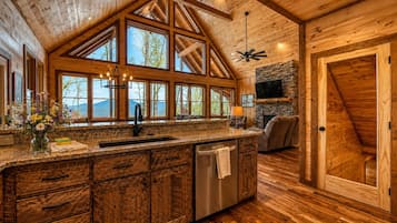 A spacious kitchen with a large island, wooden ceiling beams, and a stone fireplace.
