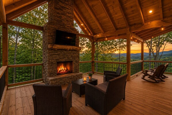 Una terraza techada al aire libre con chimenea de piedra, mobiliario de mimbre y vistas al paisaje.