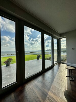 Une pièce spacieuse dotée de grandes portes-fenêtres coulissantes donnant sur un balcon avec vue sur la mer et un espace verdoyant.