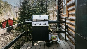 An outdoor grill setup on a wooden deck with a view of a forested area. - The Rexford Cabin: Easy Drive to PA Grand Canyon! (Gaines Township)