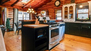 A log cabin kitchen with a central island stove, built-in oven, and a clock on the wall. - The Rexford Cabin: Easy Drive to PA Grand Canyon! (Gaines Township)