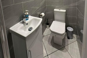 A bathroom with a white sink, toilet, and trash bin. - Studio Flat in London (London)