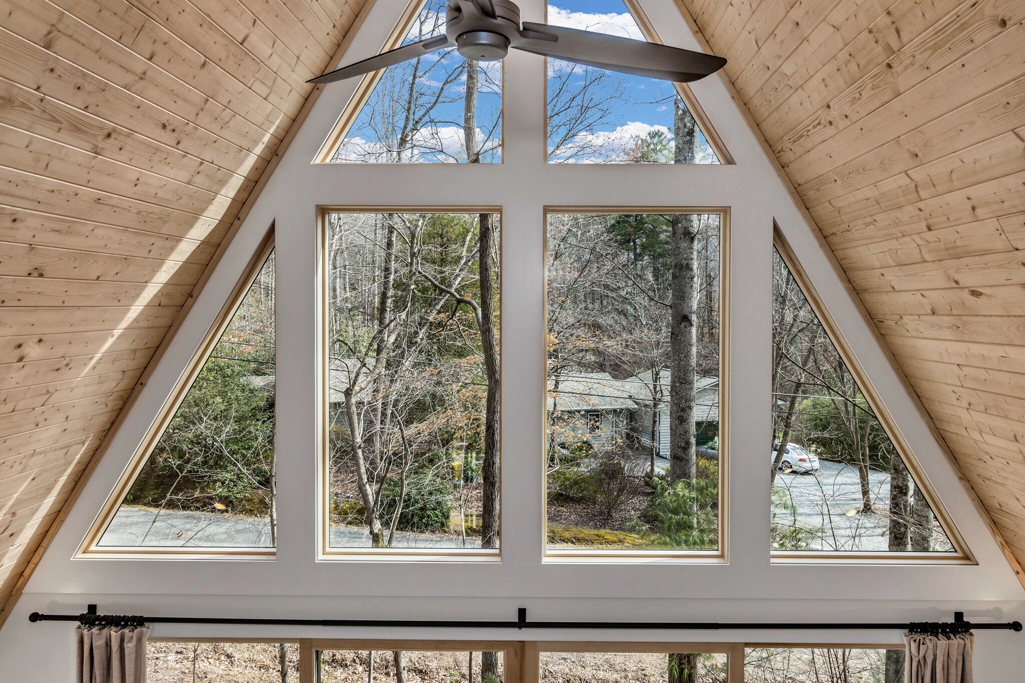 A room with a sloped wooden ceiling, large windows, and a ceiling fan.