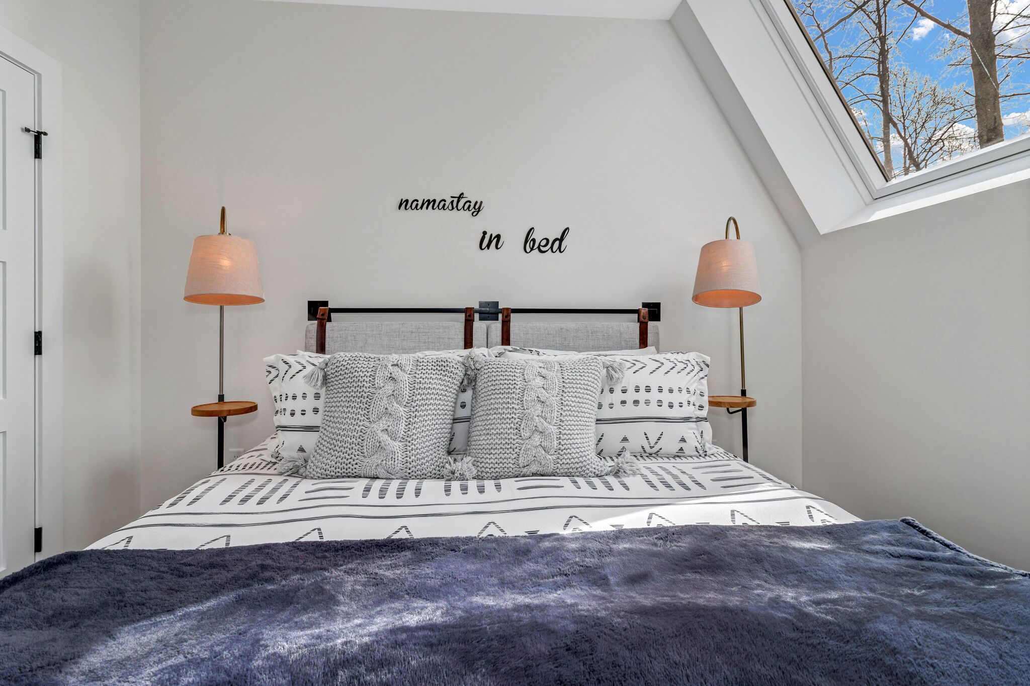 A bedroom with a bed, two bedside lamps, a wall-mounted sign, and a skylight.