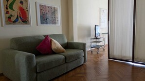 A living room with a green sofa, two cushions, a TV on a stand, and a whiteboard on the wall. - Luxury suite off Piazza del Popolo (Roma)
