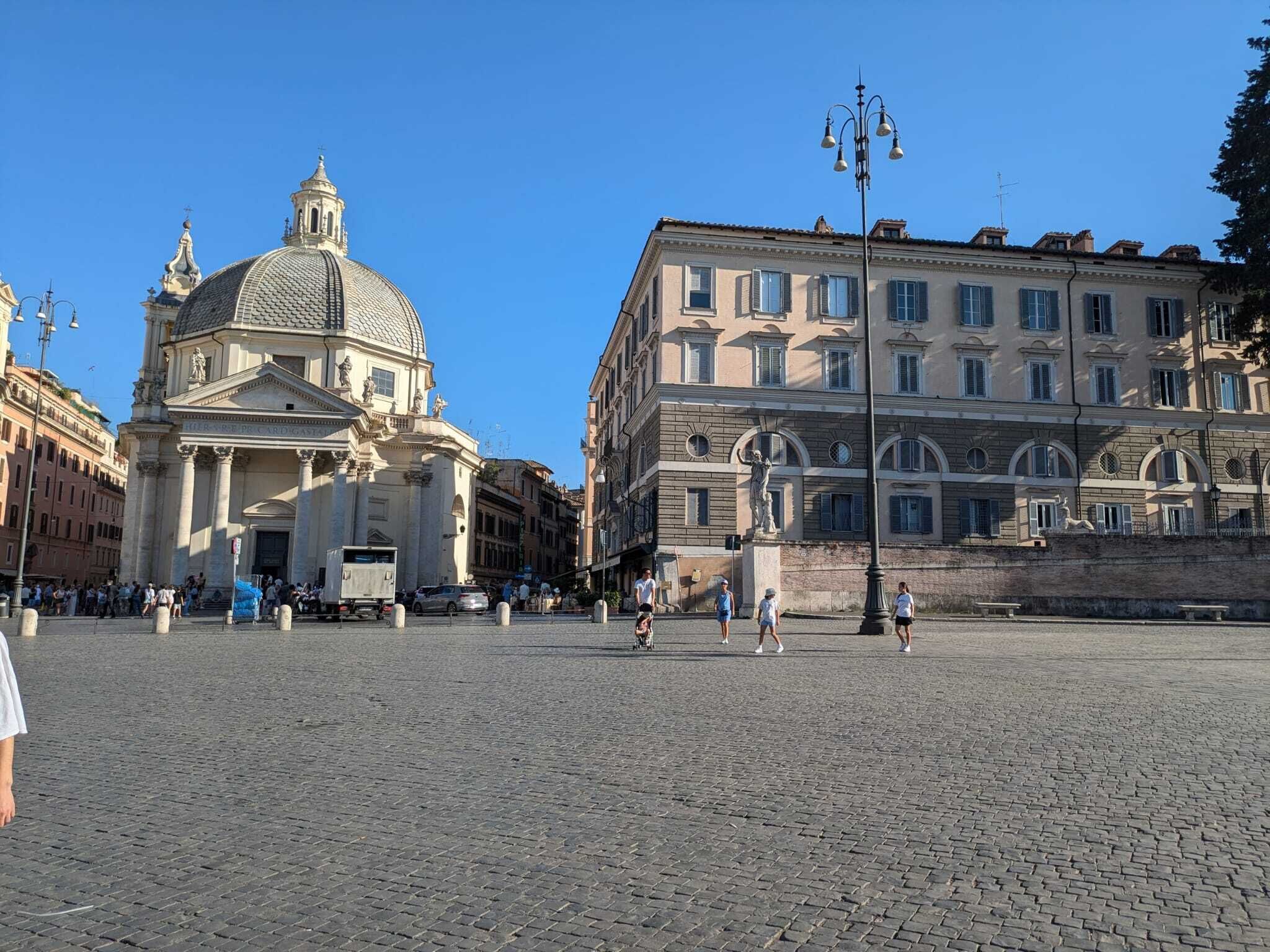 A historic square with cobblestone pavement, a prominent church with a dome, and classical architecture.