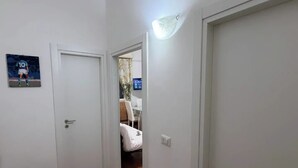 A narrow hallway with white doors, a wooden floor, and a light fixture on the wall.