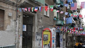 A building with a large arched doorway, a mural on the wall, and multiple flags hanging above.