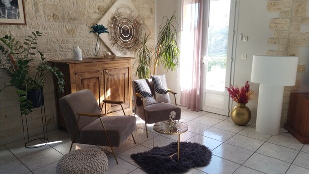 Un salon comprenant un canapé, deux fauteuils, une table basse et un meuble. On y trouve également des plantes, un tableau et une lampe.