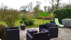 Une terrasse extérieure avec des meubles en osier, une plante en pot et un barbecue couvert.