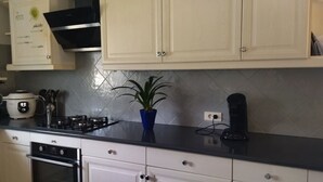 Une cuisine avec des meubles blancs, une cuisinière à gaz, une machine à café et une plante en pot.