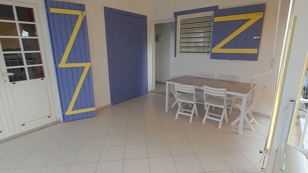 Ein Zimmer mit Fliesenboden, einem weißen Tisch mit Stühlen und blauen und gelben Wanddekorationen.