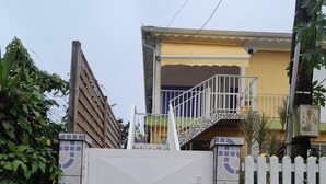 Ein verschlossenes Tor mit Fliesenmuster, ein weißer Zaun und ein Gebäude mit Balkon im Hintergrund.