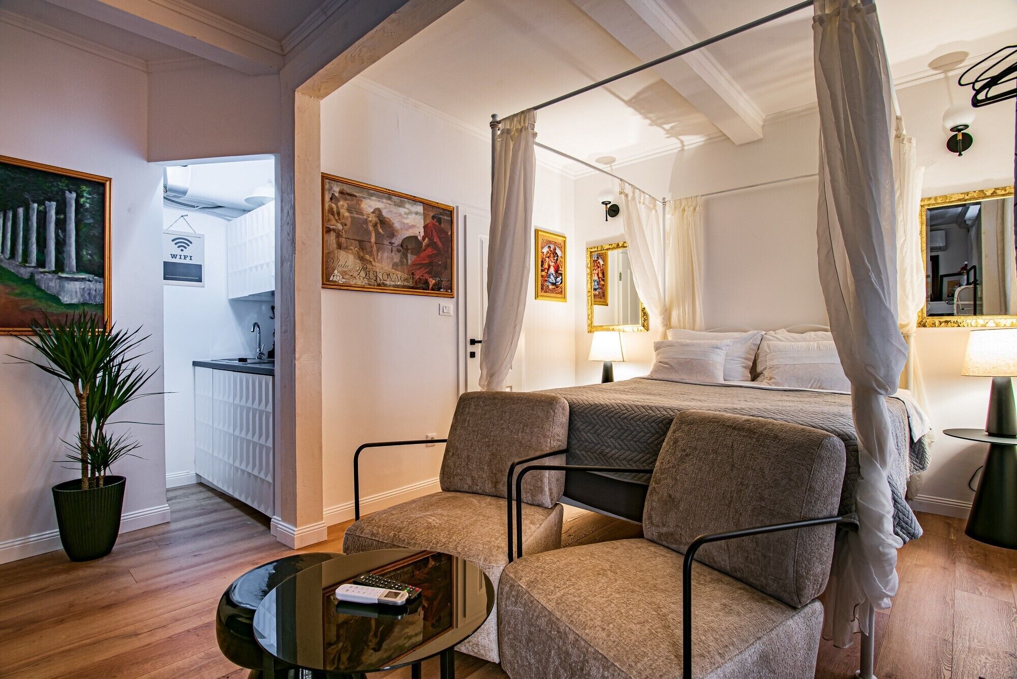 A bedroom with a four-poster bed, a sitting area with two chairs, a small table, and a potted plant.