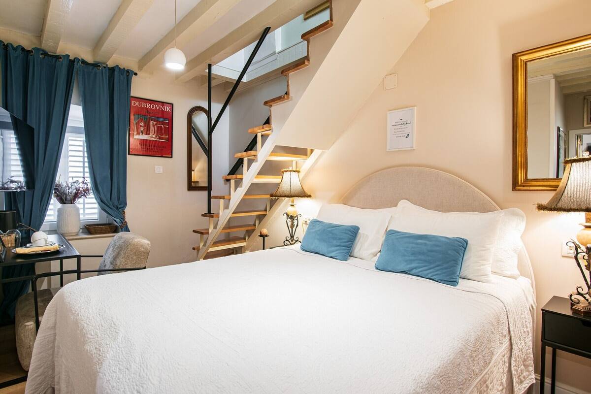 A bedroom with a large bed, a wooden staircase, a desk, and a chair.