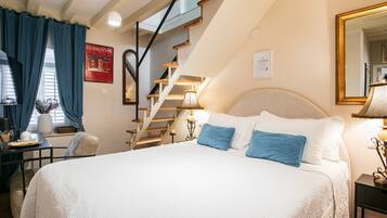 A bedroom with a large bed, a wooden staircase, a desk, and a chair.