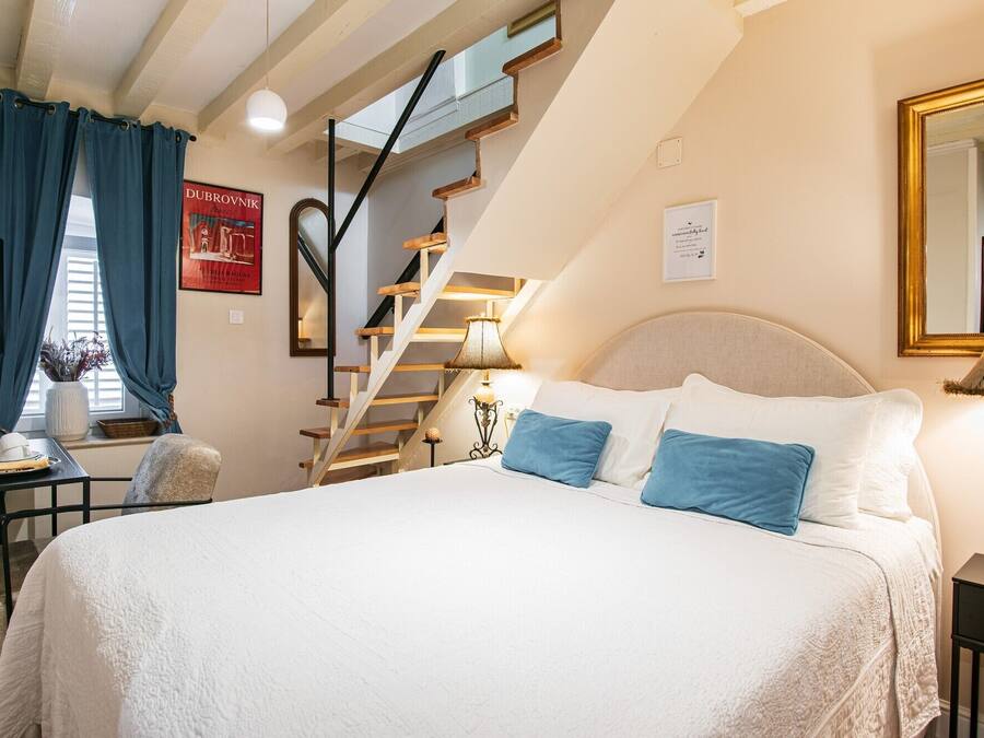 A bedroom with a large bed, a wooden staircase, a desk, and a chair.