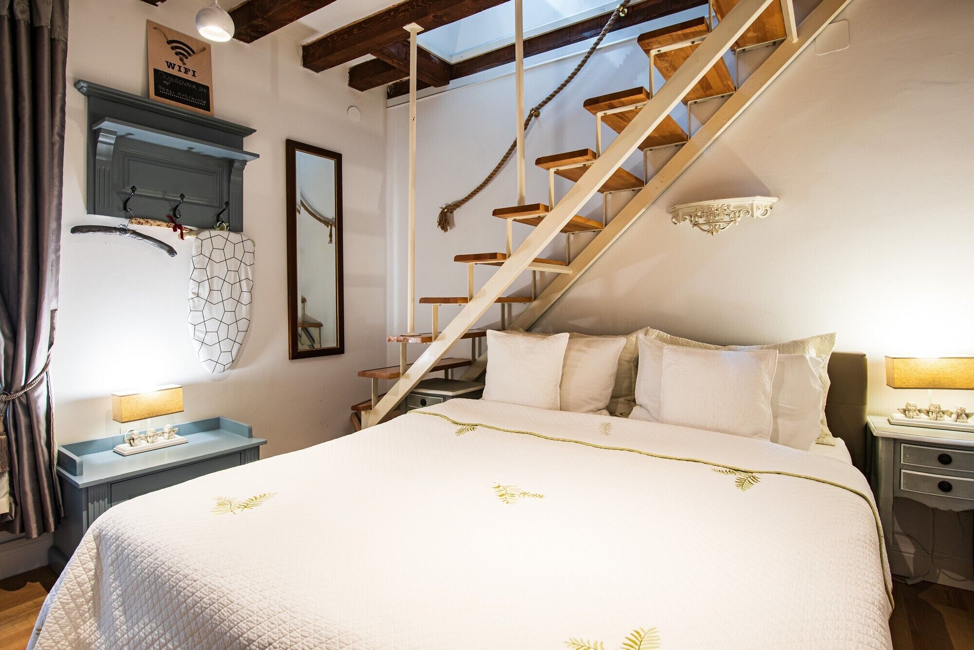 Quarto com cama, escada de madeira, espelho e luminária na parede.