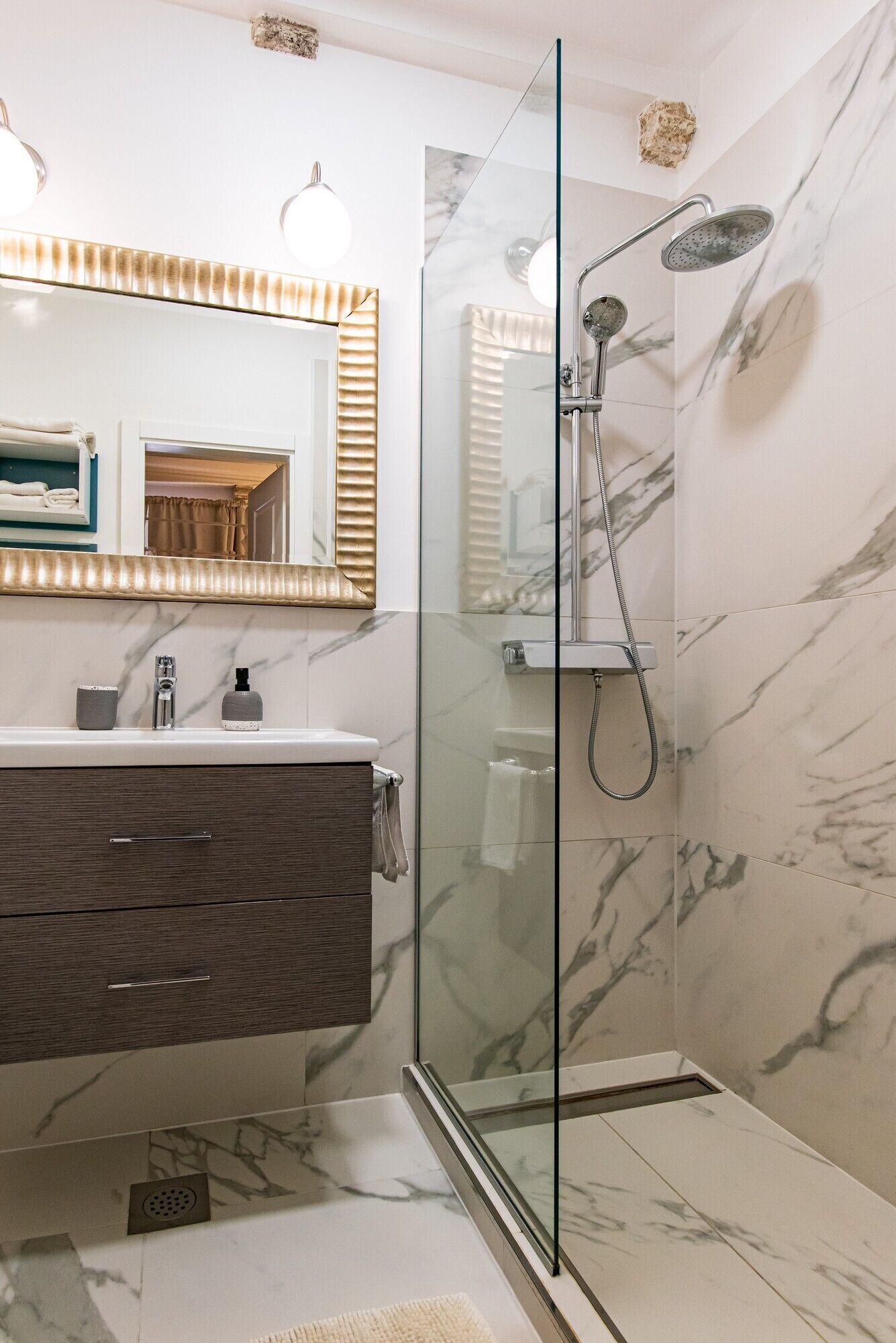 Een moderne badkamer met een douchecabine van glas, marmeren wanden en een wastafel met spiegel.