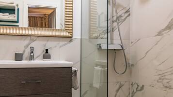 Een moderne badkamer met een douchecabine van glas, marmeren wanden en een wastafel met spiegel.