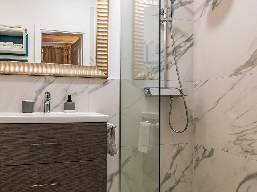 Een moderne badkamer met een douchecabine van glas, marmeren wanden en een wastafel met spiegel.