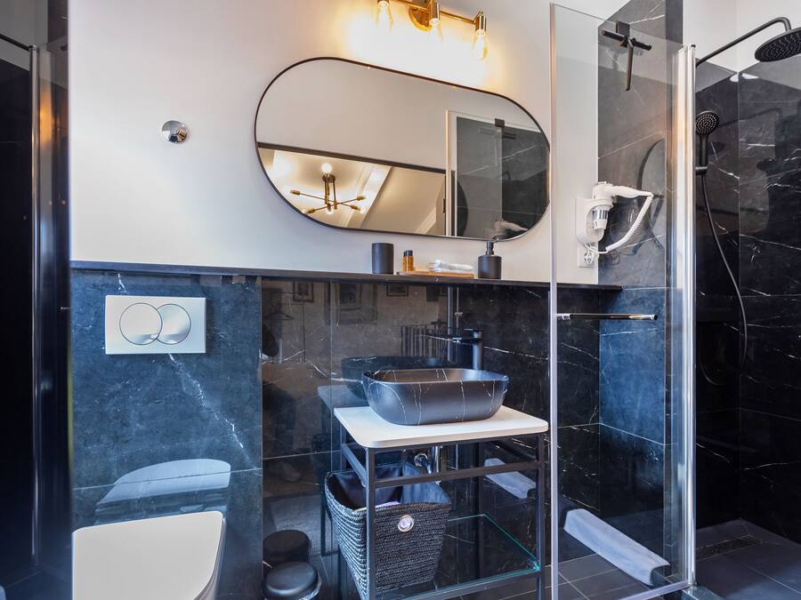 Un baño moderno con cabina de ducha de vidrio, un espejo grande y encimera de mármol.
